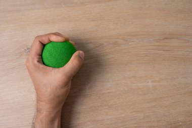 Ofisteki masada yeşil stres topunu sıkan bir adamın elleri.