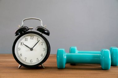 Alarm saati ve gri arka plan, spor ve sağlıklı konsept ile dambıl çalışma zamanı.