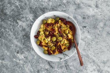 Kurutulmuş domates ve üzerine kişniş tohumları ve biber taneleri konmuş zeytinlerle vegan baharatlı kuskus, sağlıklı bitki temelli yemek tarifleri.