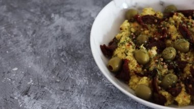 Kurutulmuş domates ve üzerine kişniş tohumları ve biber taneleri konmuş zeytinlerle vegan baharatlı kuskus, sağlıklı bitki temelli yemek tarifleri.
