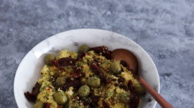 Kurutulmuş domates ve üzerine kişniş tohumları ve biber taneleri konmuş zeytinlerle vegan baharatlı kuskus, sağlıklı bitki temelli yemek tarifleri.