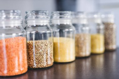 İçinde kinoa mercimek, karabuğday ve arpanın da bulunduğu farklı türde tahıl ve baklagillerin bulunduğu açık kiler kavanozları mutfak tezgahı, basit malzeme konsepti.