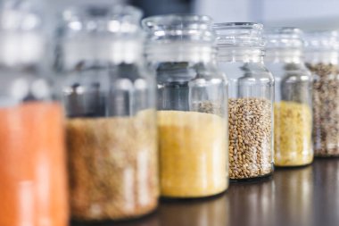 İçinde kinoa mercimek, karabuğday ve arpanın da bulunduğu farklı türde tahıl ve baklagillerin bulunduğu açık kiler kavanozları mutfak tezgahı, basit malzeme konsepti.