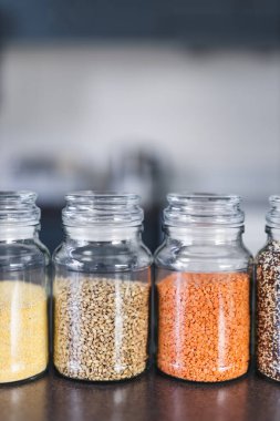 İçinde kinoa mercimek, karabuğday ve arpanın da bulunduğu farklı türde tahıl ve baklagillerin bulunduğu açık kiler kavanozları mutfak tezgahı, basit malzeme konsepti.