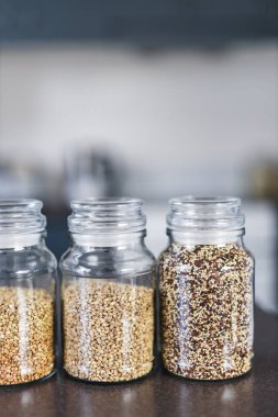 İçinde kinoa mercimek, karabuğday ve arpanın da bulunduğu farklı türde tahıl ve baklagillerin bulunduğu açık kiler kavanozları mutfak tezgahı, basit malzeme konsepti.