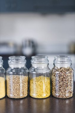 İçinde kinoa mercimek, karabuğday ve arpanın da bulunduğu farklı türde tahıl ve baklagillerin bulunduğu açık kiler kavanozları mutfak tezgahı, basit malzeme konsepti.