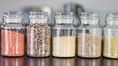 İçinde kinoa mercimek, karabuğday ve arpanın da bulunduğu farklı türde tahıl ve baklagillerin bulunduğu açık kiler kavanozları mutfak tezgahı, basit malzeme konsepti.