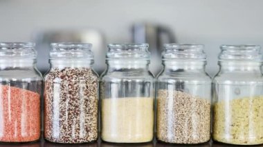 İçinde kinoa mercimek, karabuğday ve arpanın da bulunduğu farklı türde tahıl ve baklagillerin bulunduğu açık kiler kavanozları mutfak tezgahı, basit malzeme konsepti.