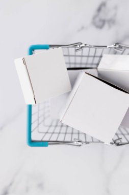 Alışveriş ve araba konseptine ekleme, alışveriş sepetinin içinde yığılmış farklı şekiller hafif mermer arka plan çekimi sığ alan derinliği