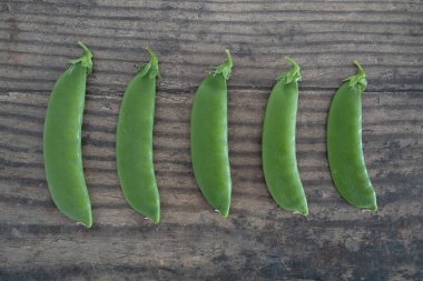 Taze toplanmış bezelyeler ahşap yemek masasında büyükten küçüğe sıralanmış, basit doğal sağlıklı malzemeler kavramı.