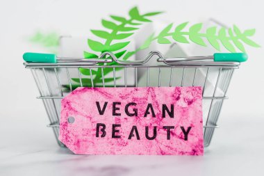 Kozmetik ve zulüm içermeyen ürün konsepti, boş ürün paketleriyle alışveriş septi ve üzerinde Vegan Güzellik etiketi olan yeşil yapraklar.
