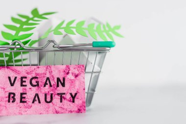 Kozmetik ve zulüm içermeyen ürün konsepti, boş ürün paketleriyle alışveriş septi ve üzerinde Vegan Güzellik etiketi olan yeşil yapraklar.