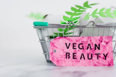 Kozmetik ve zulüm içermeyen ürün konsepti, boş ürün paketleriyle alışveriş septi ve üzerinde Vegan Güzellik etiketi olan yeşil yapraklar.