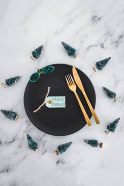 Noel süsleri mermer masa, sağlıklı beslenme ve vejetaryen Noel yemeği konseptiyle siyah yemek tabağının üzerinde bitki bazlı etiketler.