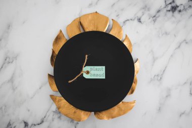 Siyah yemek tabağının üstünde altın yaprak süslemesi mermer masa, sağlıklı beslenme konsepti ve etik seçimler.