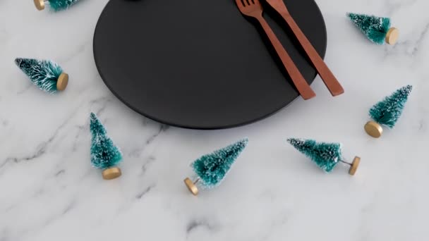 大理石のテーブルの上にクリスマスの装飾が施された黒いダイニングプレートの上に黄金のカトラリー お祝いの季節と休日の食事の概念 — ストック動画