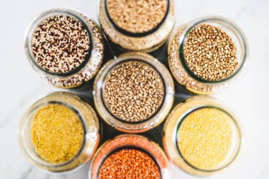 Arpa ve diğer sağlıklı tam tahıllar ve baklagiller açık kiler kavanozlarında mermer arka planda, basit vegan malzemeleri konsepti, basit vejetaryen kiler malzemeleri konsepti