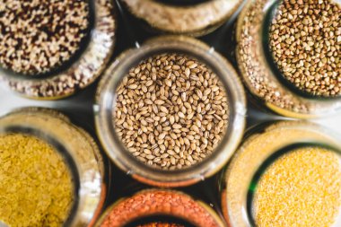 Arpa ve diğer sağlıklı tam tahıllar ve baklagiller açık kiler kavanozlarında mermer arka planda, basit vegan malzemeleri konsepti, basit vejetaryen kiler malzemeleri konsepti