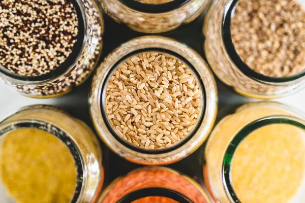 brown rice and other healthy whole grains and legumes in clear pantry jars on marble background, simple vegan pantry ingredients concept, simple vegan pantry ingredients concept