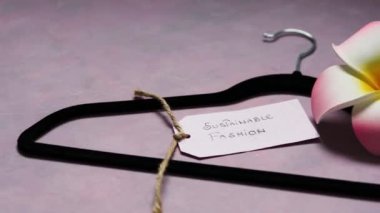 Çevreye duyarlı giyim markaları yanında tropikal frangipani çiçekleri olan pembe arka planda elbise askısı olan sürdürülebilir moda etiketleri.
