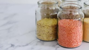 Sağlıklı tam tahıllar ve baklagiller mermer arka planda açık kiler kavanozlarında kinoa pirinç karabuğday mercimeği ve arpa, basit vejetaryen kiler malzemeleri konsepti de dahil.