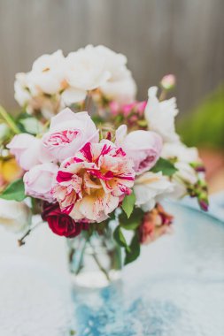 Açık hava masasının üstündeki vazoda bir demet gül çiçeği güneşli arka bahçede sığ bir tarlada çekilmiş.