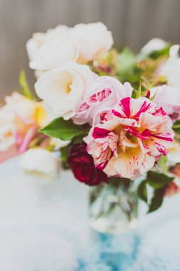 Açık hava masasının tepesindeki vazoda bir demet gül çiçeğinin sığ bir tarlada çekilmiş yakın çekimi.