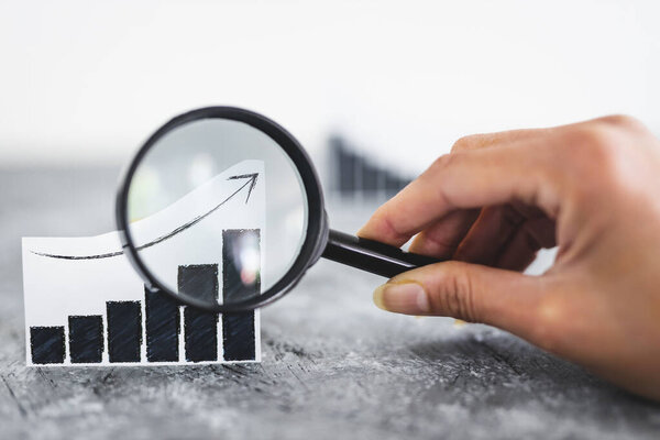 финансовые рынки или концепция денег и инвестиций, графики, показывающие тенденции вверх и вниз рядом друг с другом с увеличительным стеклом в руке, чтобы проанализировать один из них выстрелил на мелкой глубине поля