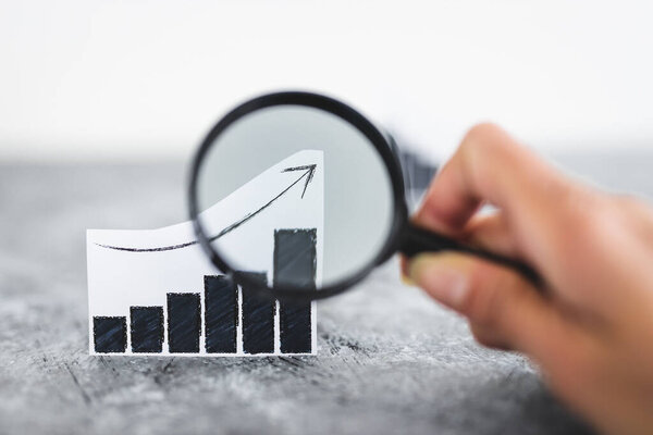 финансовые рынки или концепция денег и инвестиций, графики, показывающие тенденции вверх и вниз рядом друг с другом с увеличительным стеклом в руке, чтобы проанализировать один из них выстрелил на мелкой глубине поля