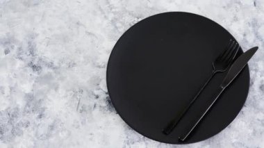 Gri arka planda çatal ve bıçaklı siyah yemek tabağı. Minimalist kompozisyon, diyet ve sezgisel yeme kavramı.