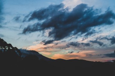 Günbatımı bulutları dağların üzerinde yuvarlanıyor ve kışın Avustralya, Tazmanya 'da yoğun bitki örtüsü çekiliyor.