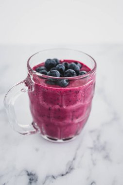 raspberry and dragonfruit smoothie with blueberries topping in pint glass on top of white marble background