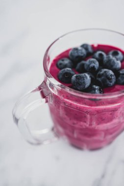 raspberry and dragonfruit smoothie with blueberries topping in pint glass on top of white marble background