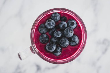 raspberry and dragonfruit smoothie with blueberries topping in pint glass on top of white marble background