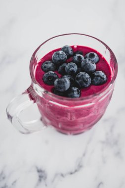 raspberry and dragonfruit smoothie with blueberries topping in pint glass on top of white marble background