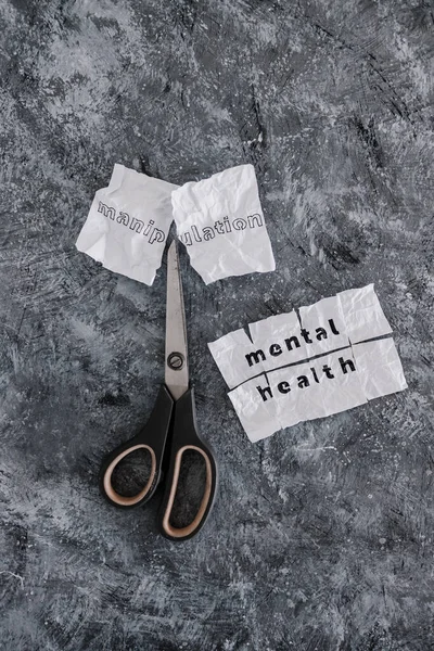 Manipulation text on crumpled piece of paper which is getting cut with scissors next to Mental Health text, concept of psychology and emotional strength to deal with toxic behaviours