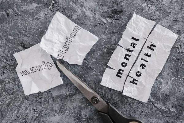 Manipulation text on crumpled piece of paper which is getting cut with scissors next to Mental Health text, concept of psychology and emotional strength to deal with toxic behaviours