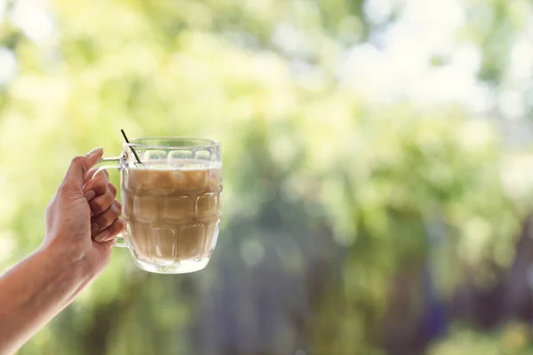 日当たりの良い裏庭のボケの前のビール スタイン グラスでアイスコーヒーを手に取る夏のリラクゼーションとドリンクのコンセプト — ストック写真