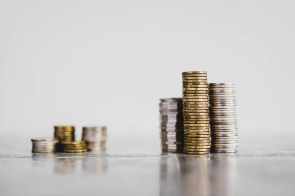 stacks of different coins divided between a small and a big group on white background, concept of good vs bad investements or before and after investing
