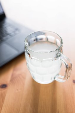 Yemek masasında dizüstü bilgisayarın yanında bira bardağında limon suyu, gün boyunca susuz kalma konsepti.