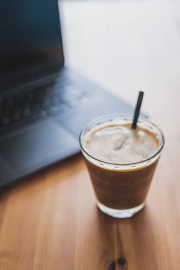 Yemek masasında dizüstü bilgisayarın yanında açık bir bardakta soya sütlü kahve, uzaktan kumanda konsepti ya da ofiste kahve molası.
