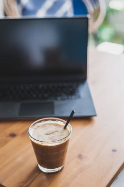 Yemek masasında dizüstü bilgisayarın yanında açık bir bardakta soya sütlü kahve, uzaktan kumanda konsepti ya da ofiste kahve molası.