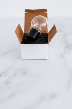 Beyaz kutunun üstünde minimalist beyaz mermer arka planda ampul fikri olan kutu kavramının dışında düşünün.