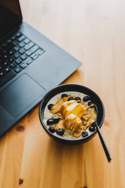 Evde dizüstü bilgisayarla çalışırken mango yulaf ezmesi yemek, uzaktan kumanda konsepti ya da ofiste öğle yemeği yemek.