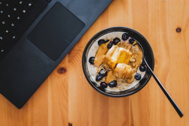 Evde dizüstü bilgisayarla çalışırken mango yulaf ezmesi yemek, uzaktan kumanda konsepti ya da ofiste öğle yemeği yemek.