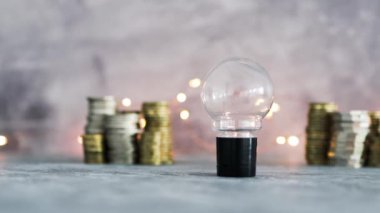 Fikir ampulü farklı altın ve gümüş para yığınları ile büyük miktarda para temsil ediyor. Peri ışığı, başarı ve bolluk kavramı ile gri beton arka planda çekim yapmak.
