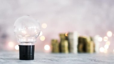 Fikir ampulü farklı altın ve gümüş para yığınları ile büyük miktarda para temsil ediyor. Peri ışığı, başarı ve bolluk kavramı ile gri beton arka planda çekim yapmak.