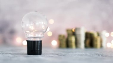Fikir ampulü farklı altın ve gümüş para yığınları ile büyük miktarda para temsil ediyor. Peri ışığı, başarı ve bolluk kavramı ile gri beton arka planda çekim yapmak.