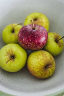 Ortasında bir kırmızı elma olan bir grup yeşil elma, sağlıklı yiyecek kavramı veya kalabalıktan dikkat çekme metaforu.