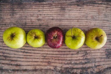 Ortasında bir kırmızı elma olan bir grup yeşil elma, sağlıklı yiyecek kavramı veya kalabalıktan dikkat çekme metaforu.
